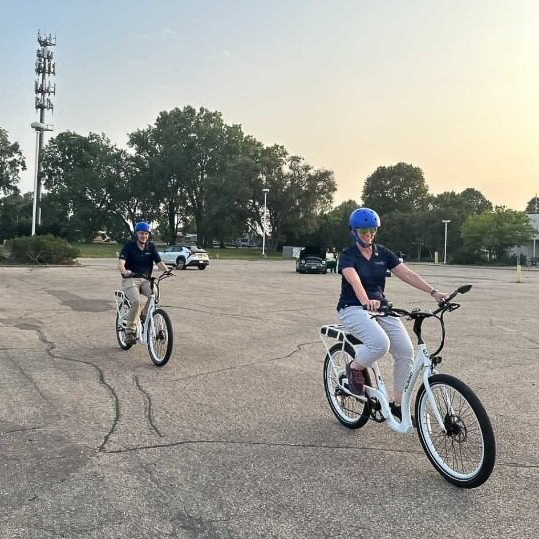 Two people riding electric bikes in an empty parking lot