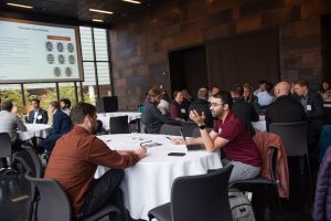 A closeup of two men having a discussion in a full room of people.